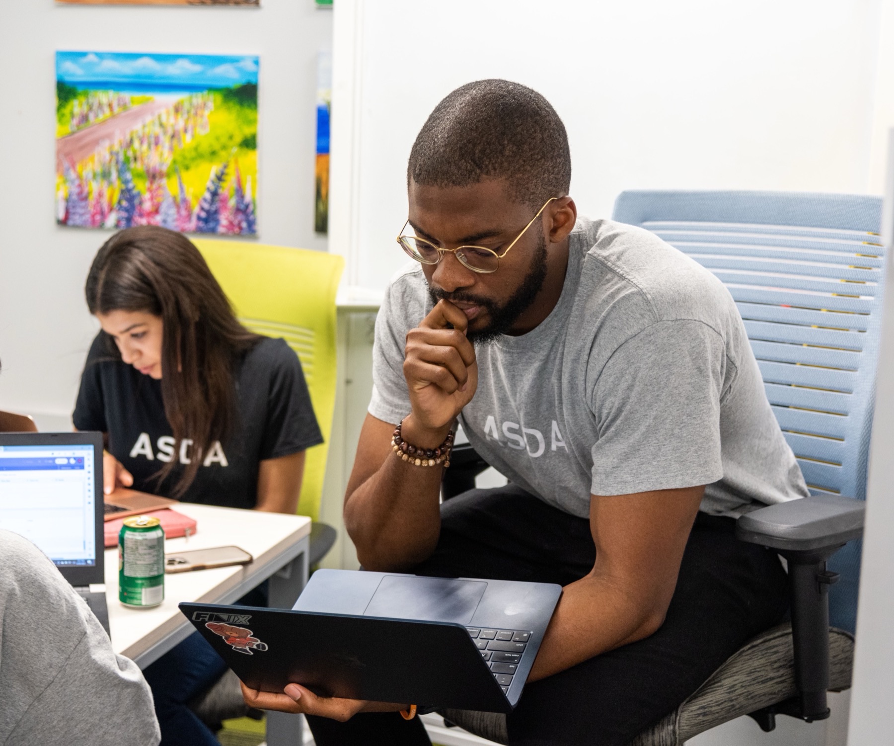 A founder thinking through work on a laptop beside two teammates at a shared table.